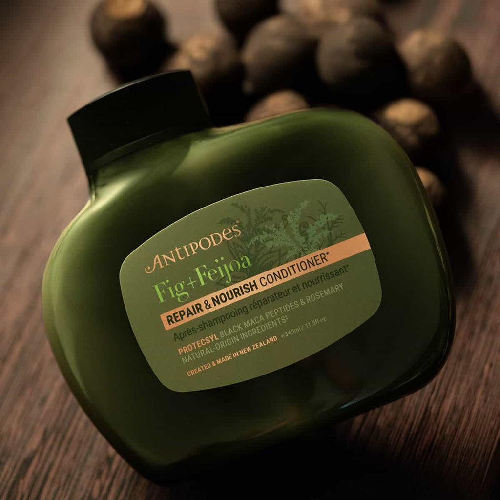 Green bottle of Antipodes Fig + Feijoa Conditioner on a wooden surface.