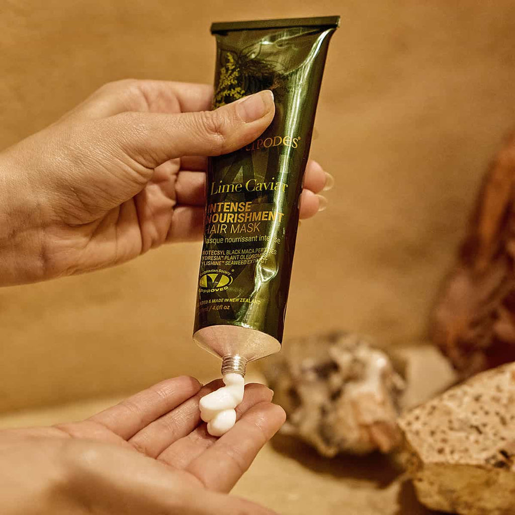 Hand holding a green skincare product tube with visible cream on a blurred background.