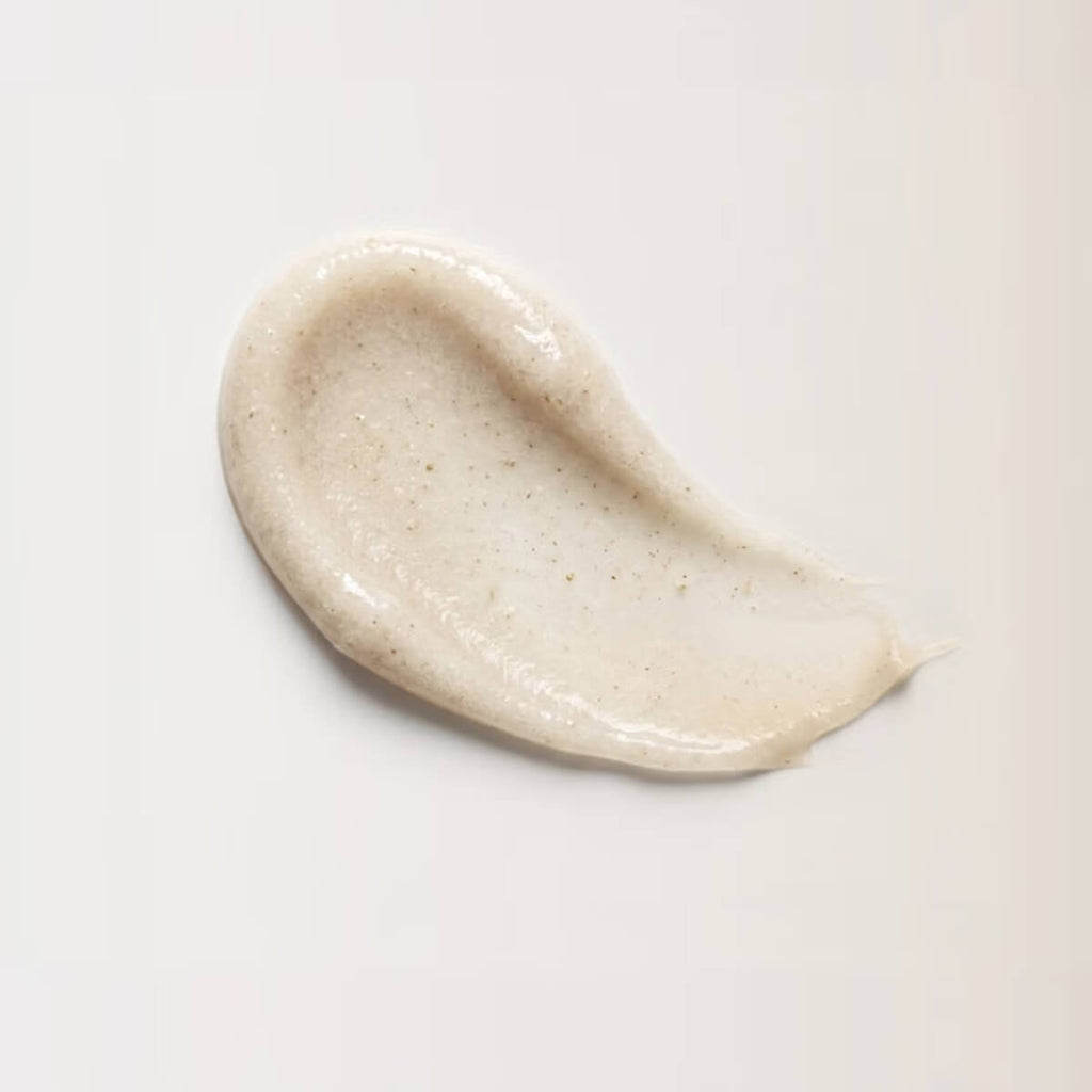 A thick, creamy beige cosmetic smear with fine brown specks, showing a smooth, glossy texture on a clean white background.