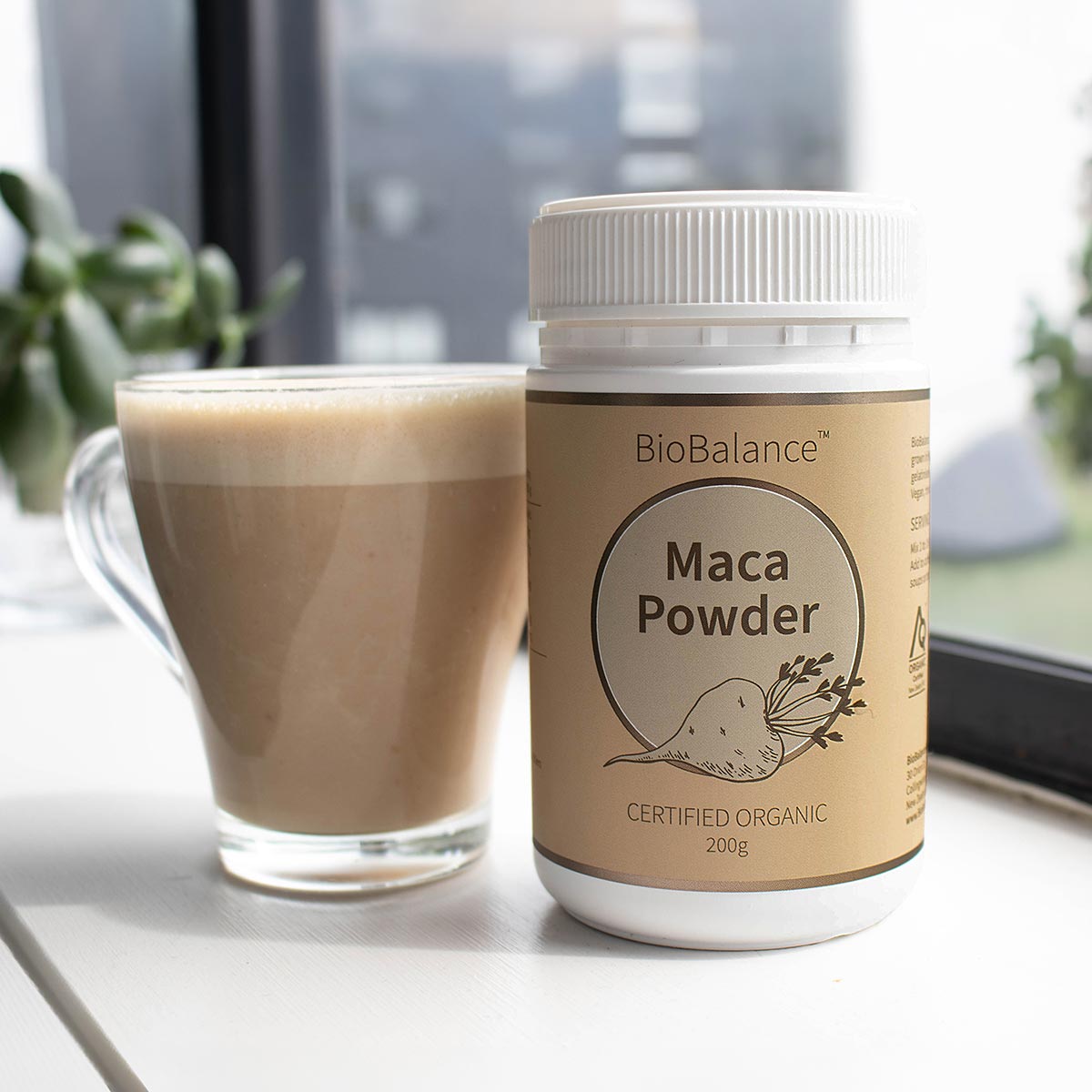Maca powder container next to a glass of a creamy looking blended drink with maca powder.
