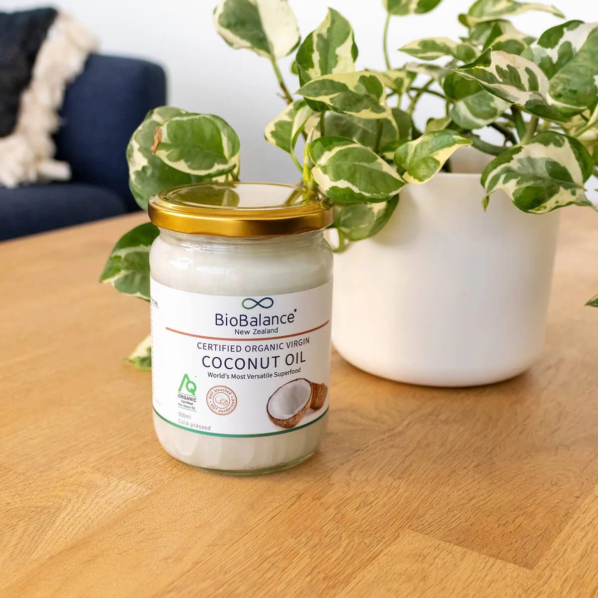Jar of BioBalance coconut oil on a wooden table with a plant in the background.
