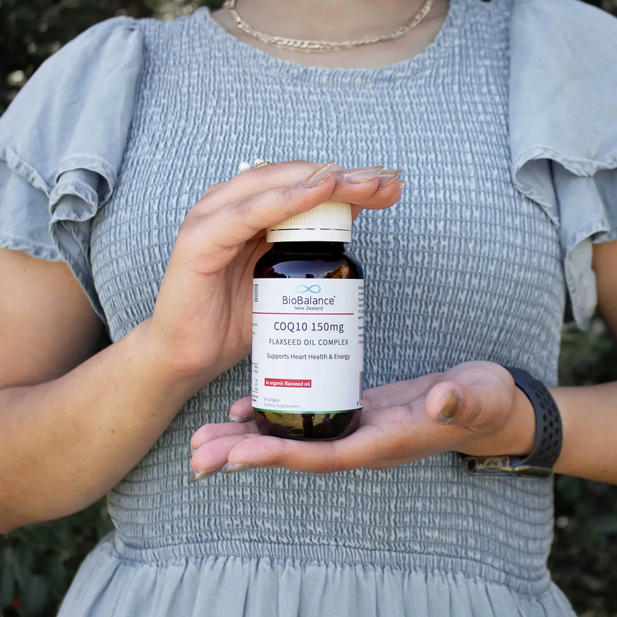 Person holding a BioBalance COQ10 150mg supplement bottle outdoors.