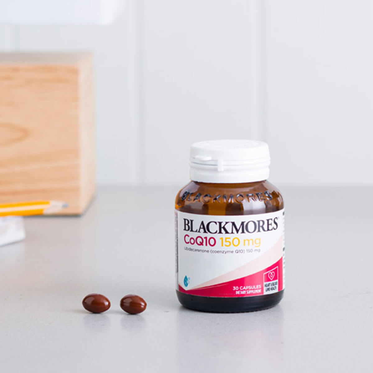 Blackmores CoQ10 supplement bottle on a white surface with a wooden block in the background.