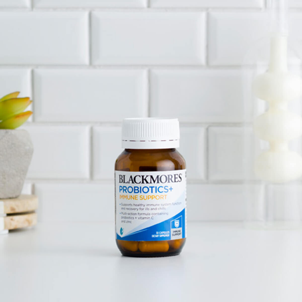 Blackmores Probiotics+ bottle on a white surface with a tiled wall background.