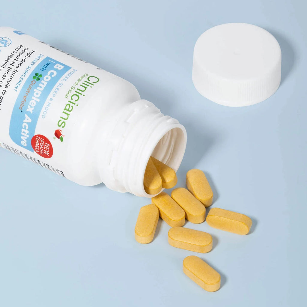 Bottle of open Clinicians B Complex Active on a blue background with yellow tablets spilling out.