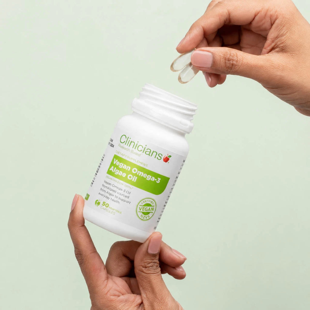 Person holding a bottle of Clinicians Vegan Omega-3 Algae Oil and showing softgel capsules.