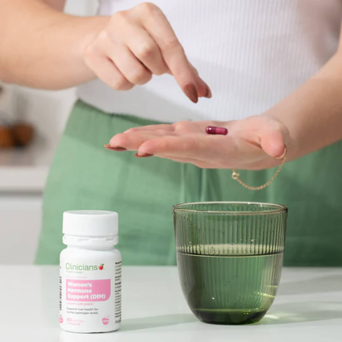 Person holding a pill with a bottle of supplements and a glass of water on a table.
