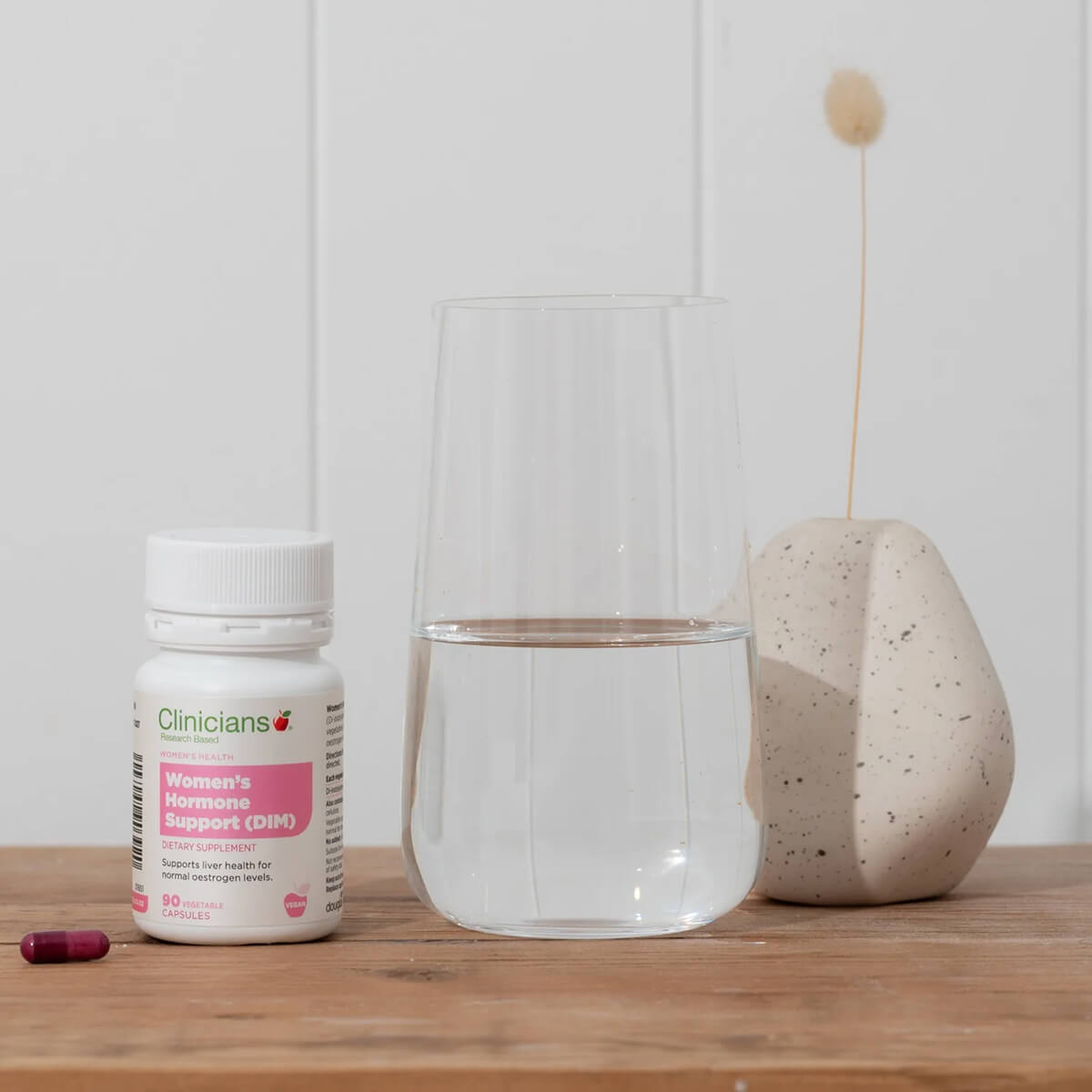 Supplement bottle labeled 'Clinicians' on a wooden surface with a glass of water and a decorative stone.