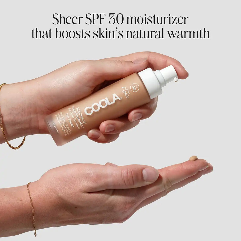 A person holds a bottle of COOLA SPF30 moisturizer against a light gray background, with text above reading 'Sheer SPF 30 moisturizer that boosts skin's natural warmth'.