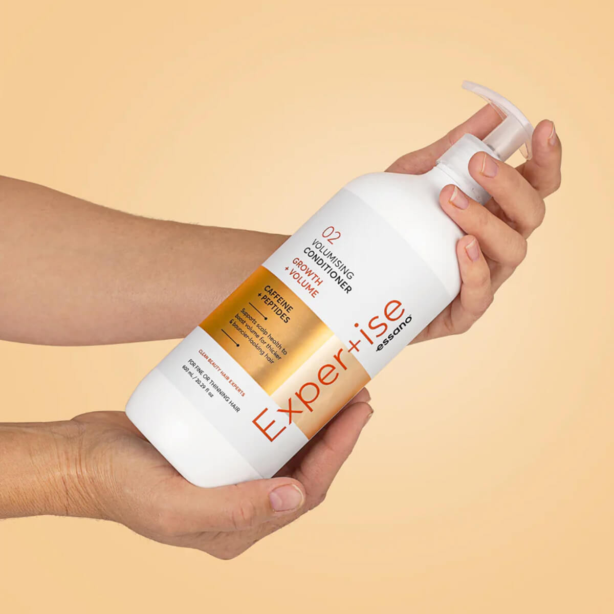Hand holding a bottle of 'Expertise' volumising conditioner against a beige background.