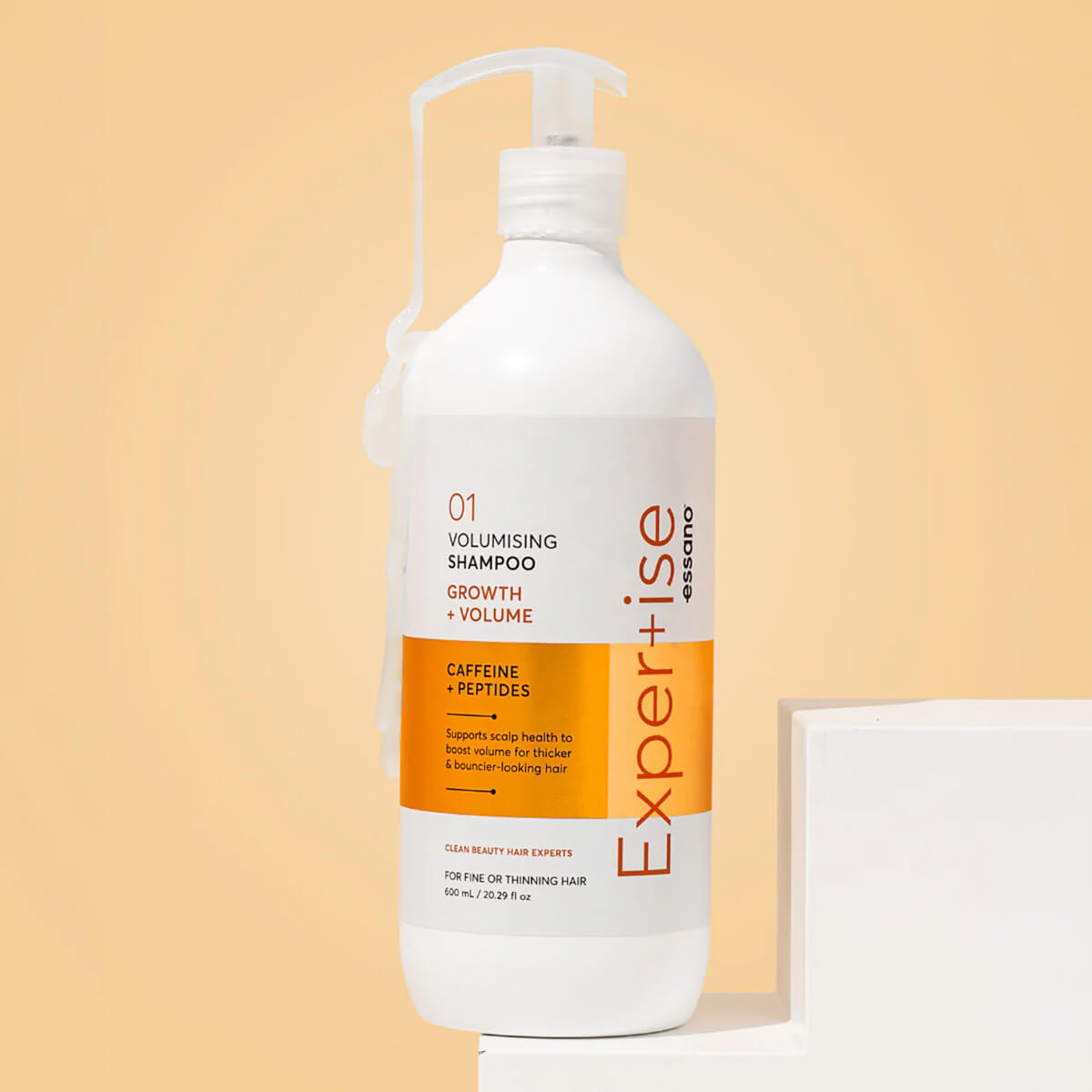 Shampoo bottle with orange label on a beige background.