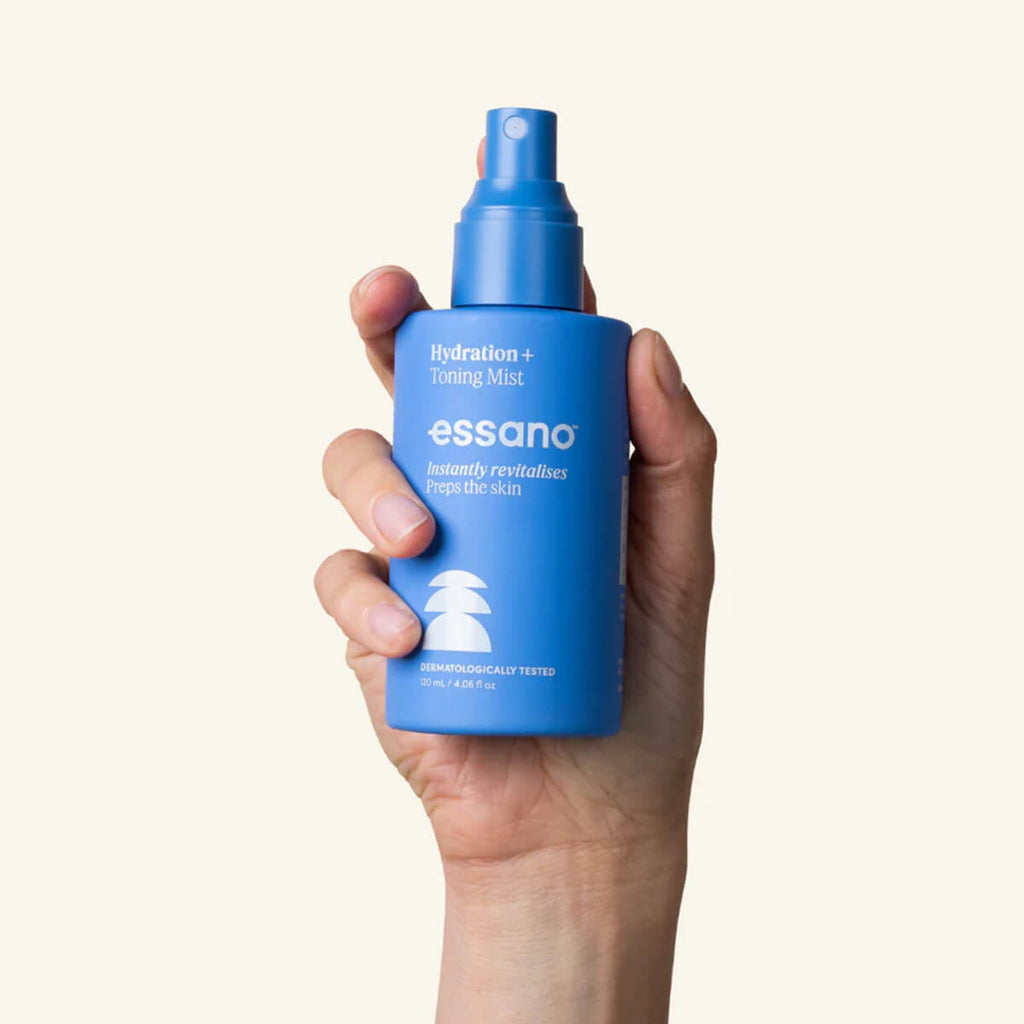 Hand holding a blue bottle of Essano hydration mist against a white background.