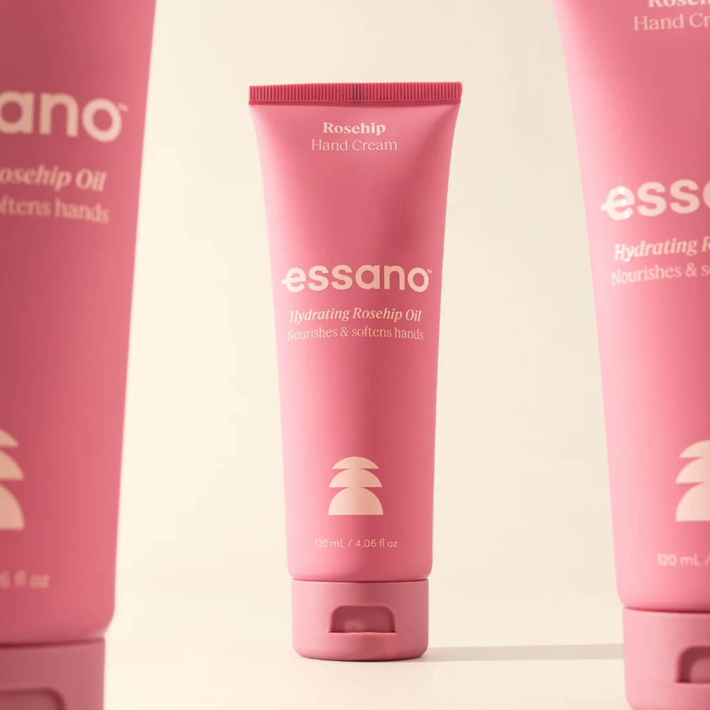 Three pink tubes of essano hand cream on a light beige background.