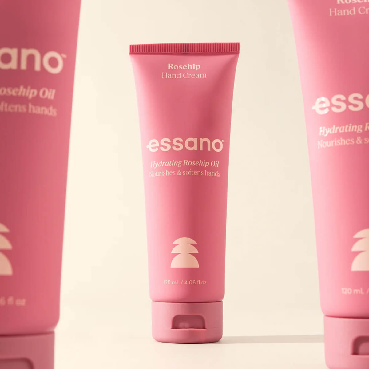 Three pink tubes of essano hand cream on a light beige background.
