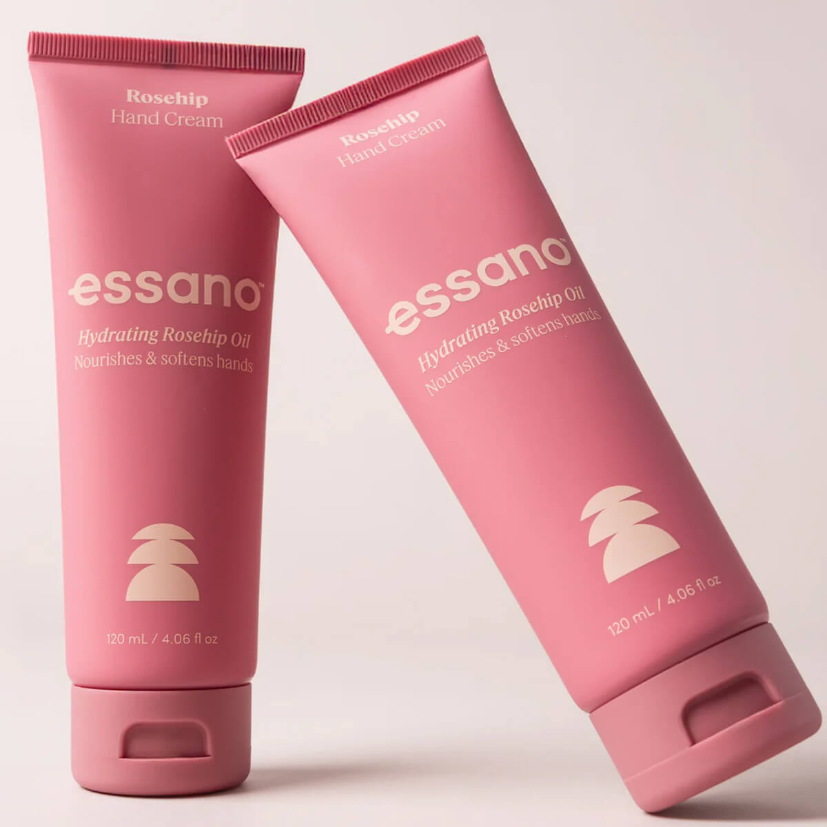 Two pink tubes of essano hand cream on a light pink background.