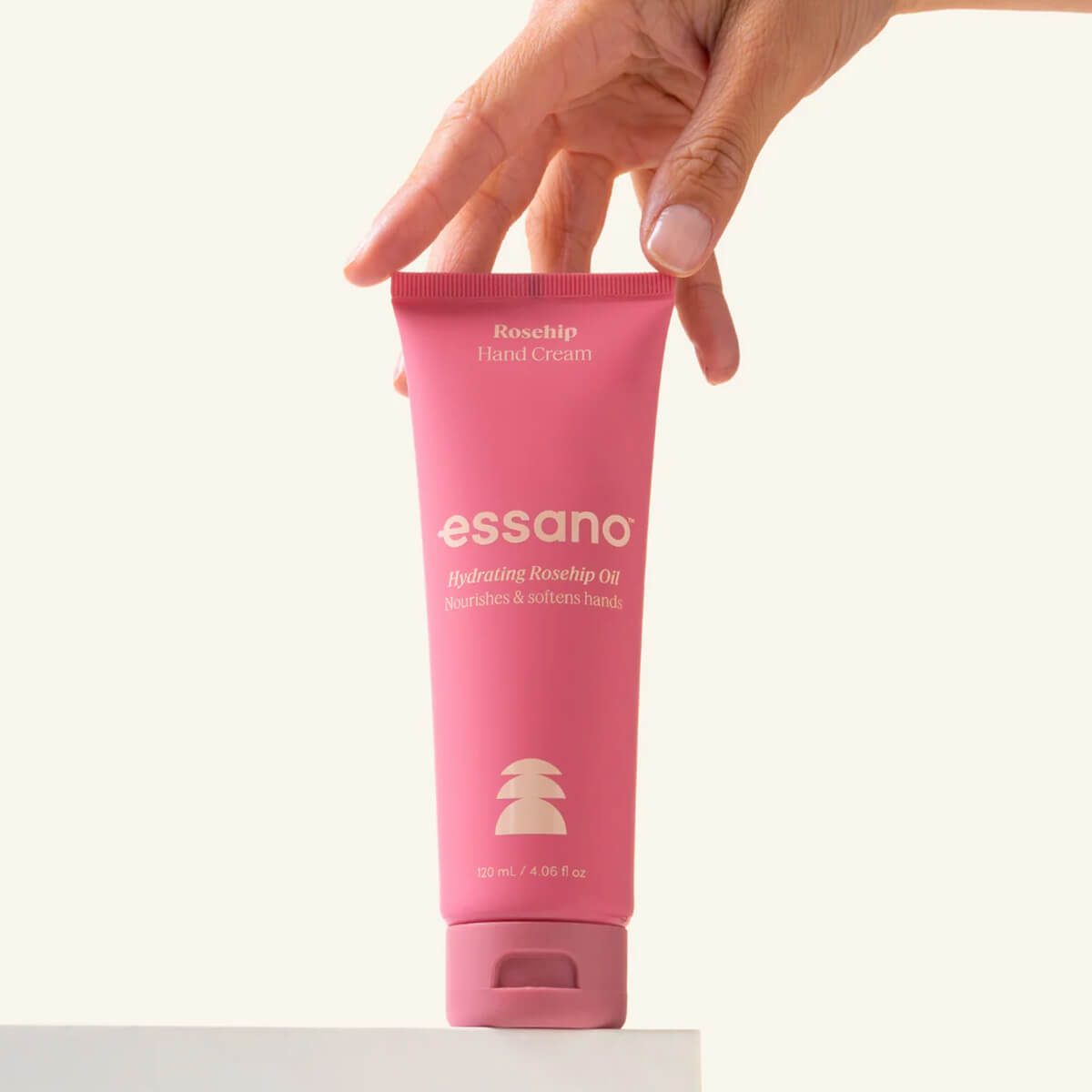 Pink tube of essano hand cream held by a hand on a white background.