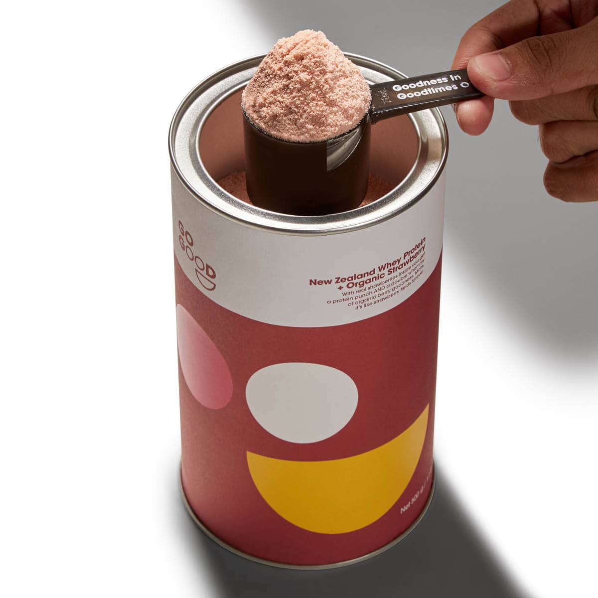 Red canister with white label being opened by a hand holding a spoonful of powder.