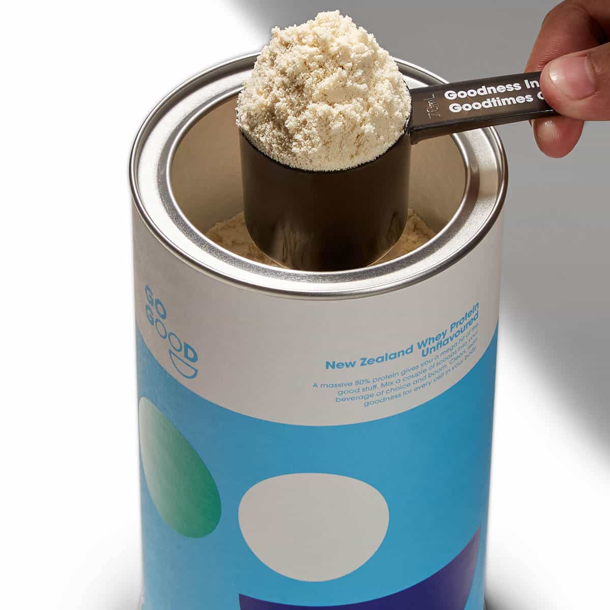Spoonful of protein powder over a container.