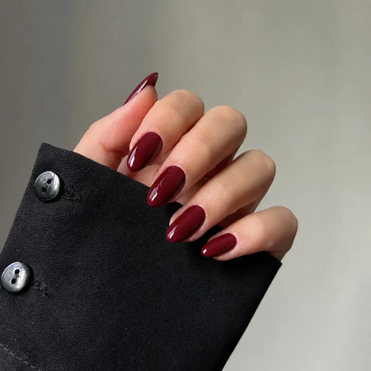 A close-up of a hand with long, glossy almond-shaped nails painted in a deep burgundy red shade.