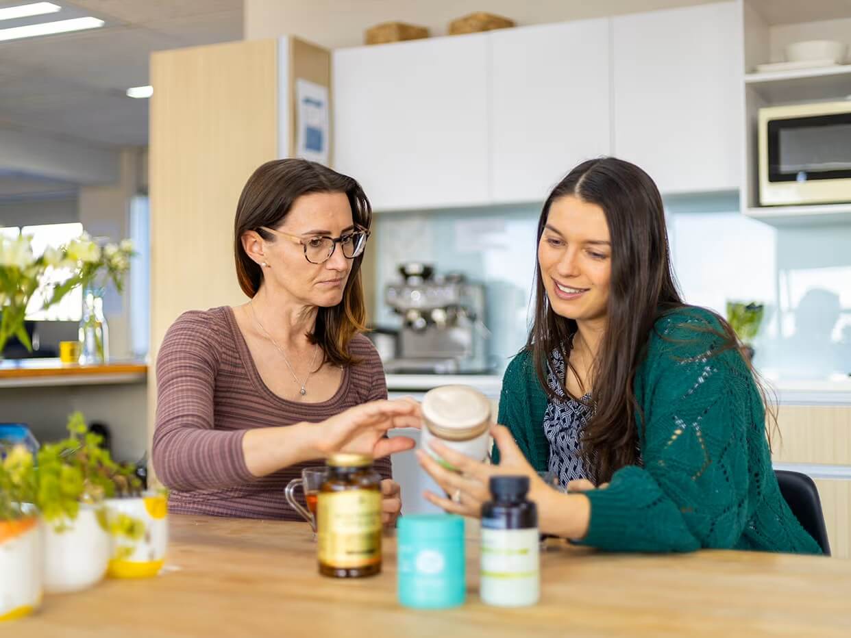 Two professional women in an office reviewing supplement products.