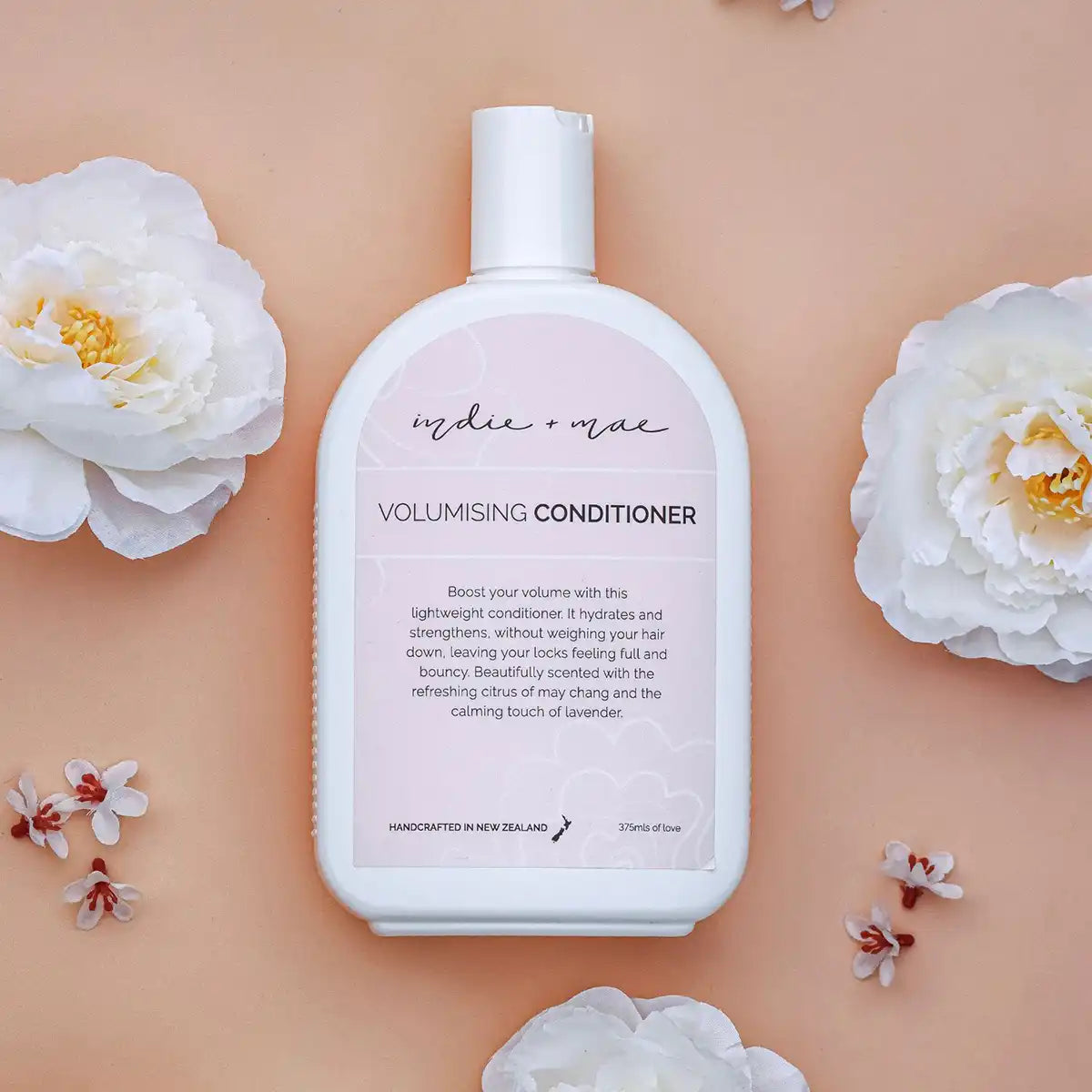 Volumising conditioner bottle with floral elements on a peach background.