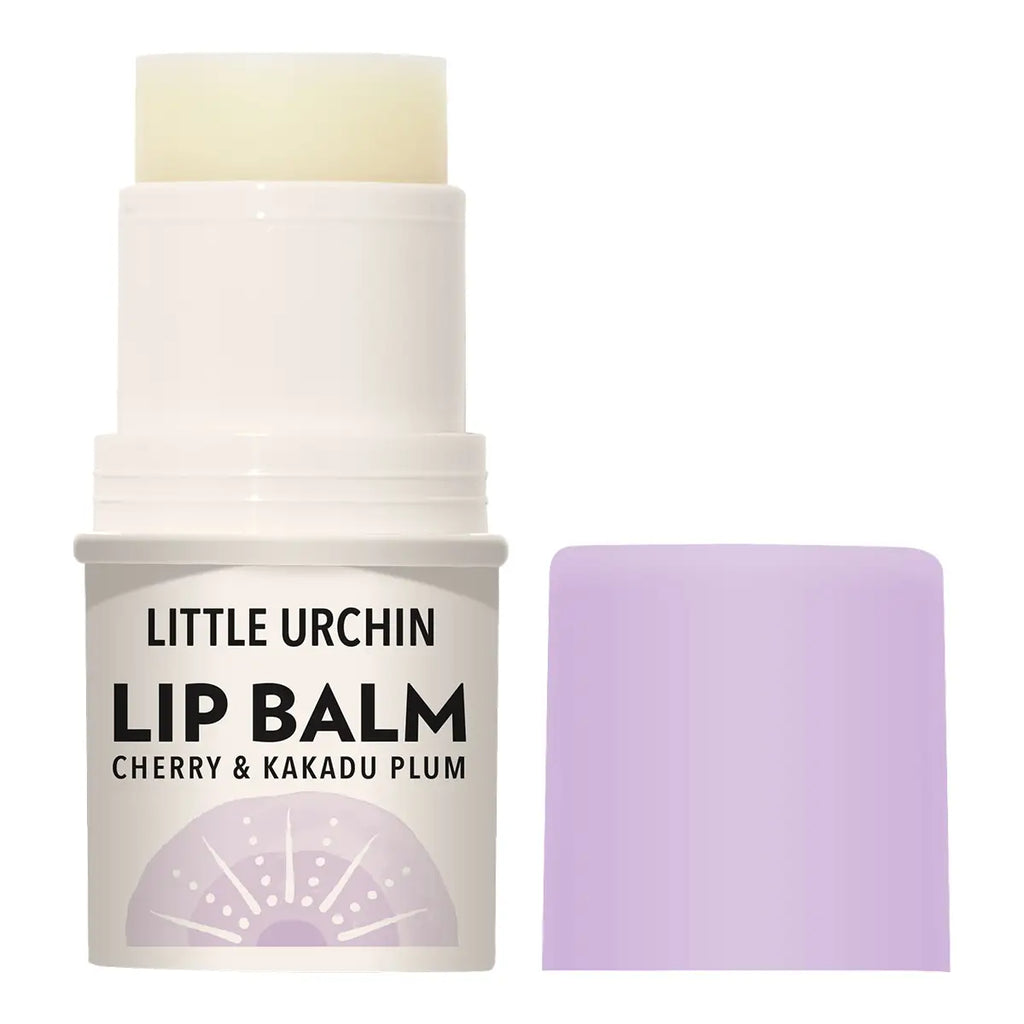 A stick of Little Urchin Lip Balm with its cap removed, showing the pale yellow balm stick and a lavender purple cap placed beside it on a white background.