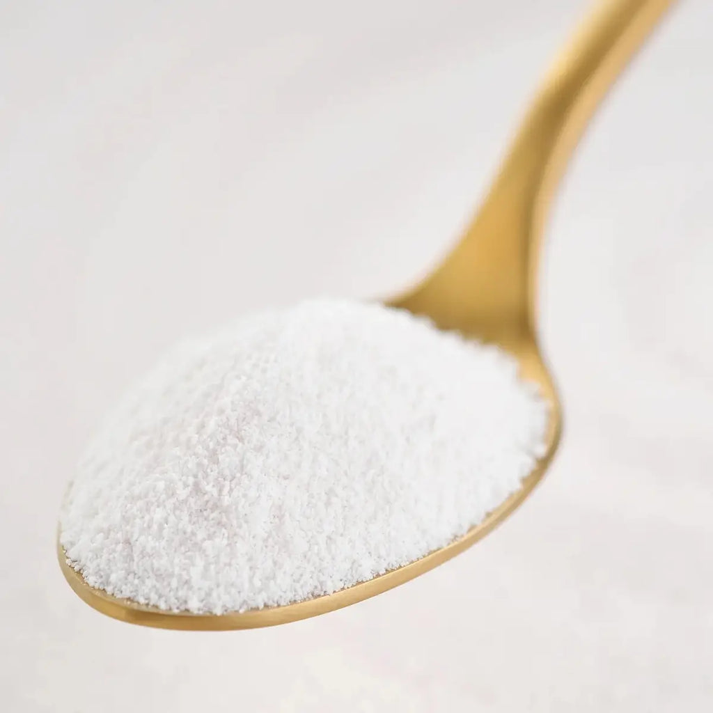 A close-up of a gold spoon filled with fine white powder, photographed against a soft light background.