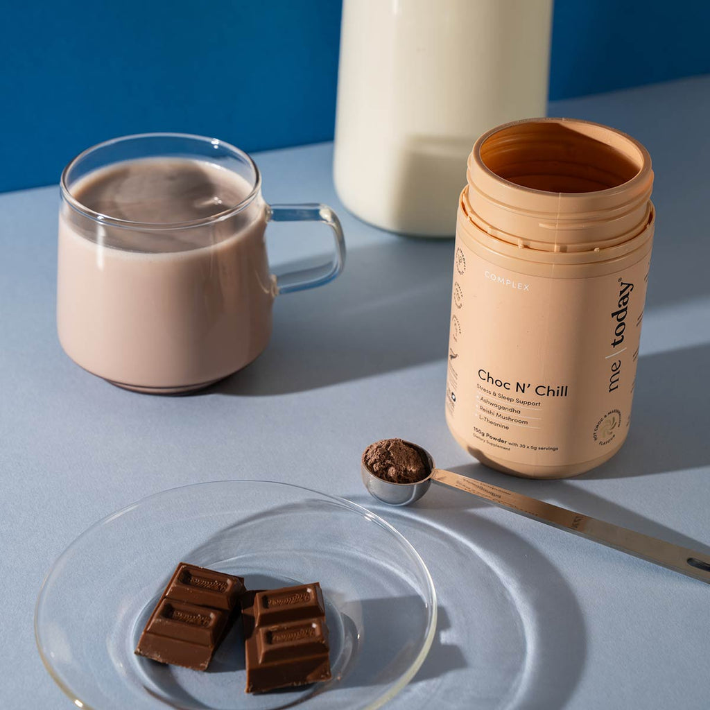 Hot chocolate with a container of 'Choc N' Chill' mix, chocolate pieces, and a spoon on a light blue surface.