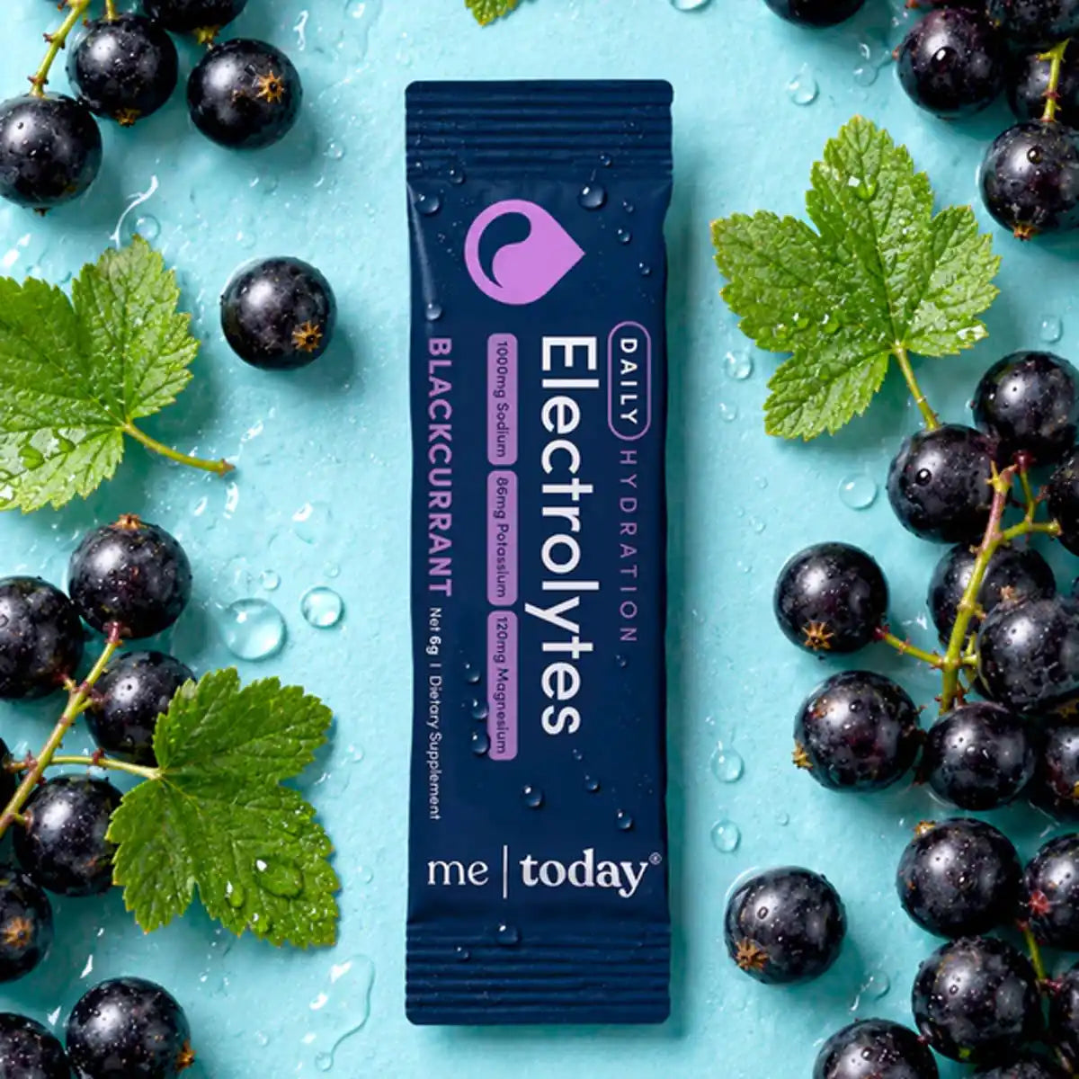 Single sachet of blackcurrant electrolytes on a blue background with freshly picked blackcurrants.