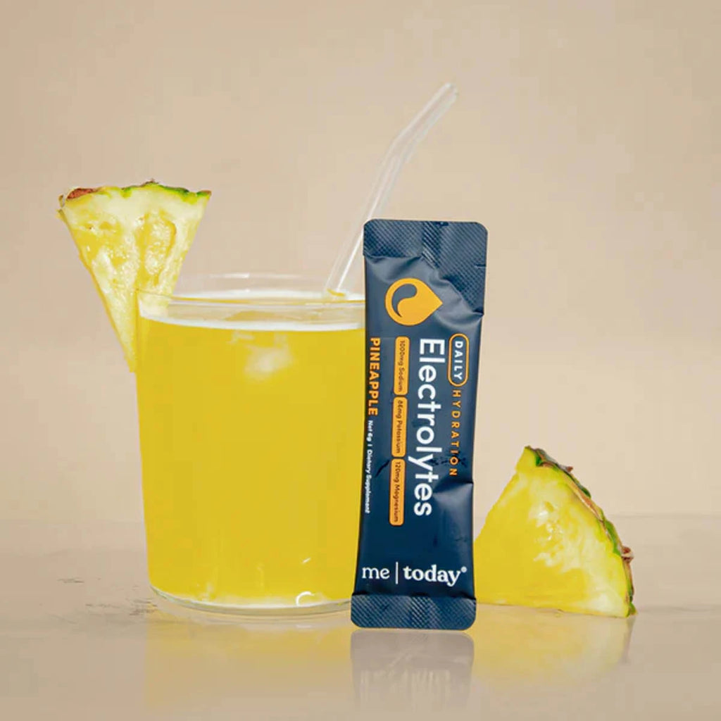 Single sachet of pineapple electrolytes next to a glass of iced yellow electrolytes with pineapple pieces.