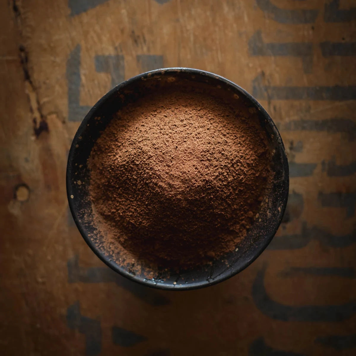 Cocoa powder in a black bowl on a cardboard background