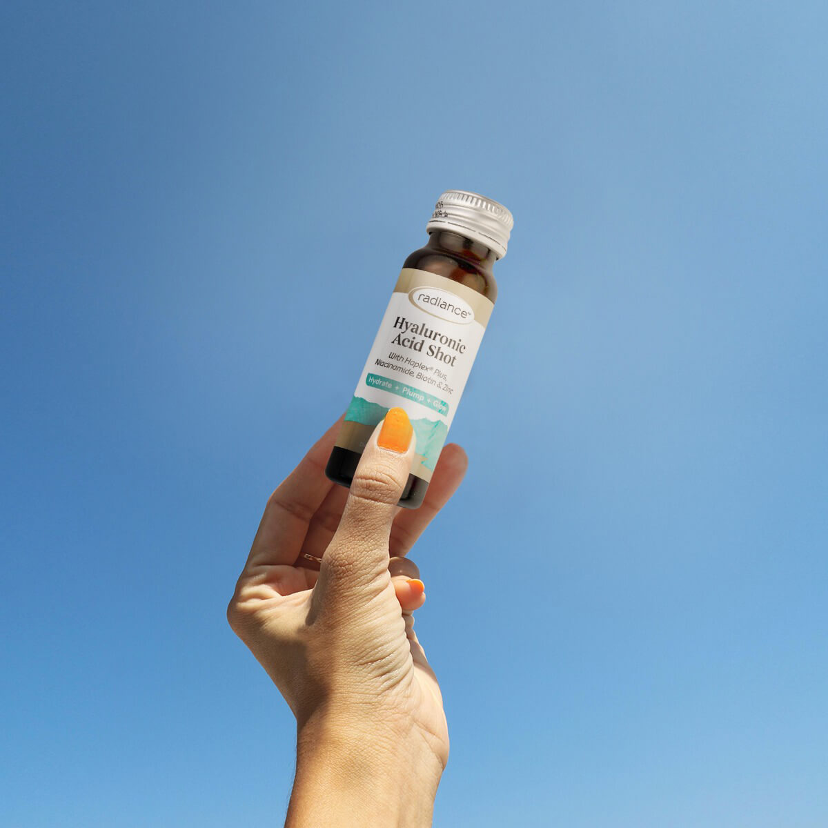 Hand holding a bottle of skincare product against a clear blue sky