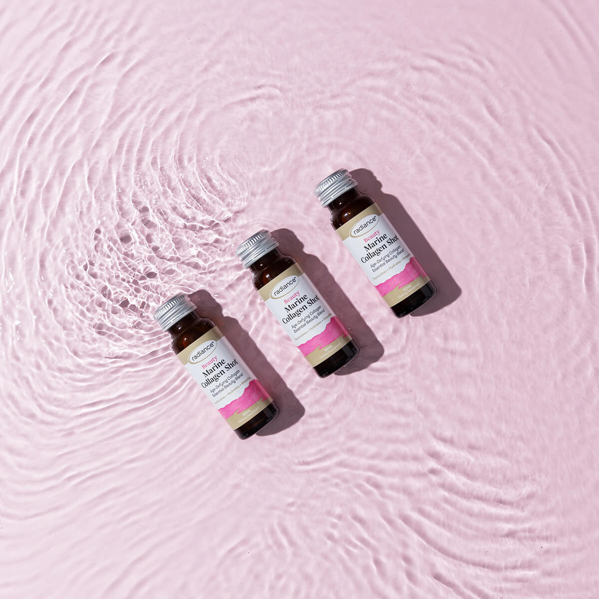 Four bottles of Collagen Shots on a pink textured background.