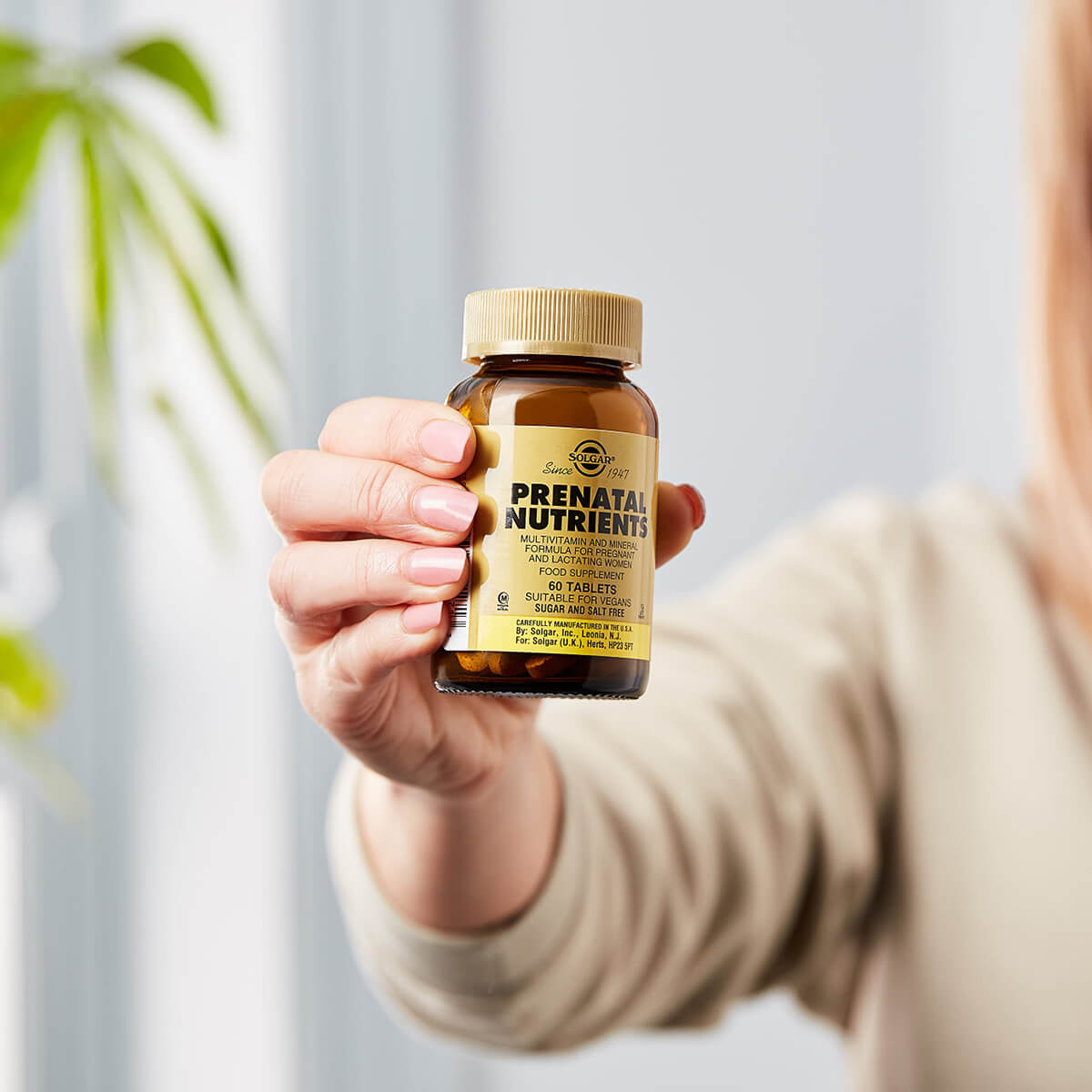 Hand holding bottle of Prenatal Nutrients supplements.