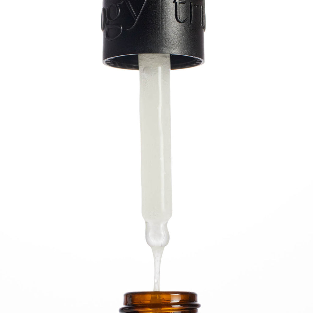 Black dropper bottle with vitamin c booster serum being dispensed on a white background