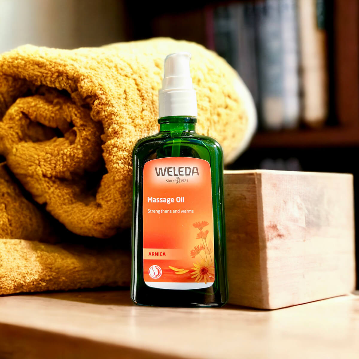 Weleda massage oil bottle with a yellow towel and wooden block on a wooden surface.